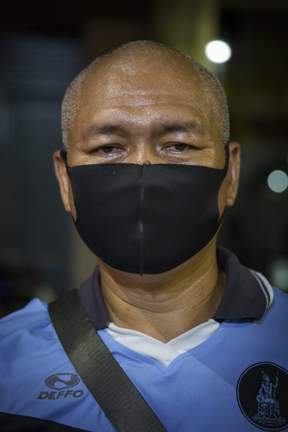 A person wearing a black mask and blue polo. 