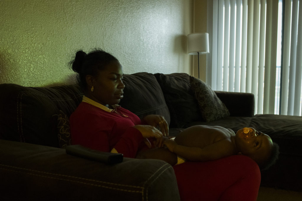 A Black woman in a red outfit sits on the couch while her son reclines in her lap. 