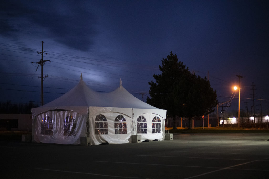 A white tent with clear plastic window stands in the middle of an empty parking lot. 