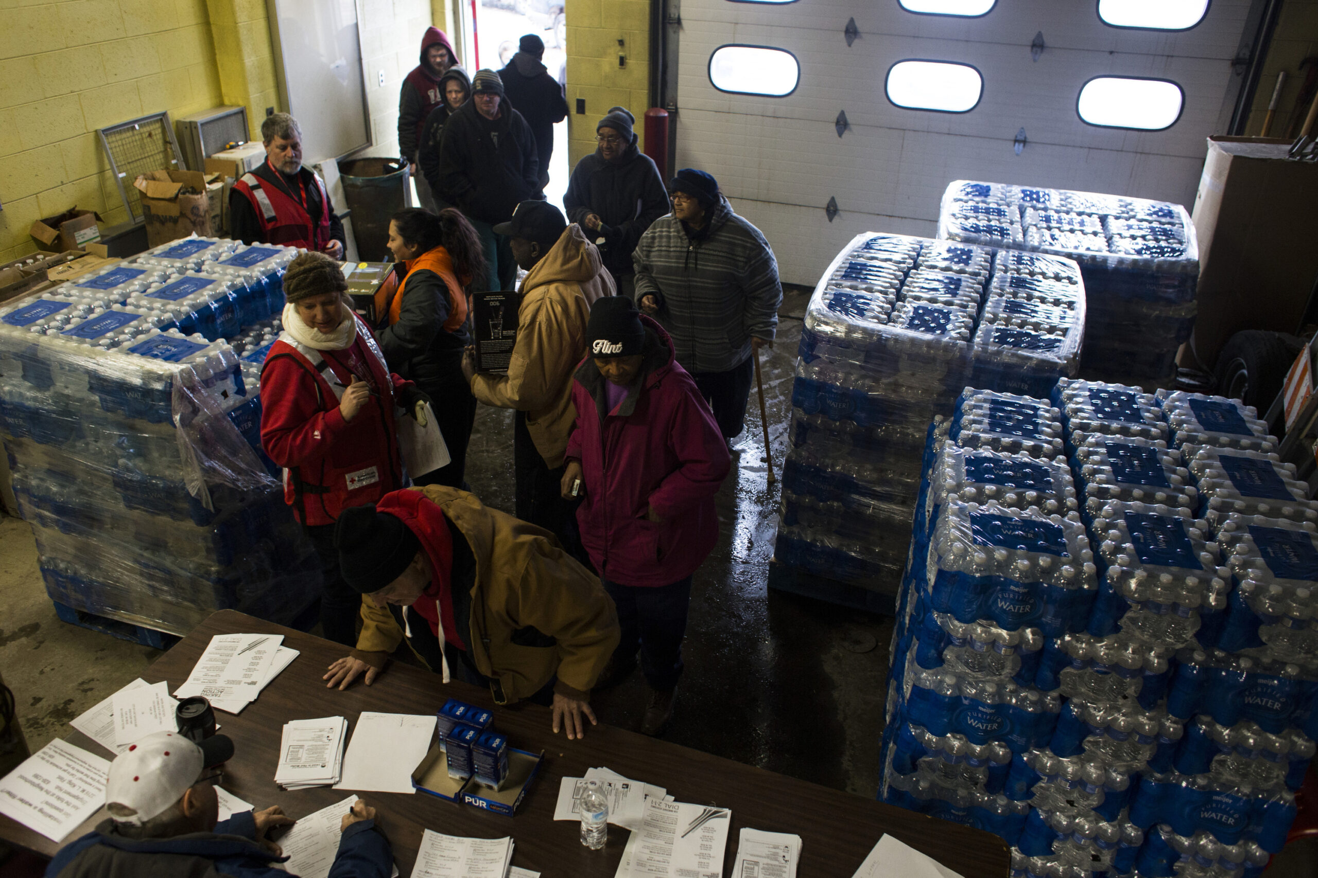 Overhead shot of inside of fire station with crowd of people surrounded by stacks of water bottles