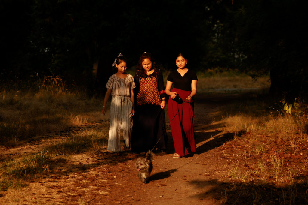 A woman and her two daughters walks their dog on a dirt path.