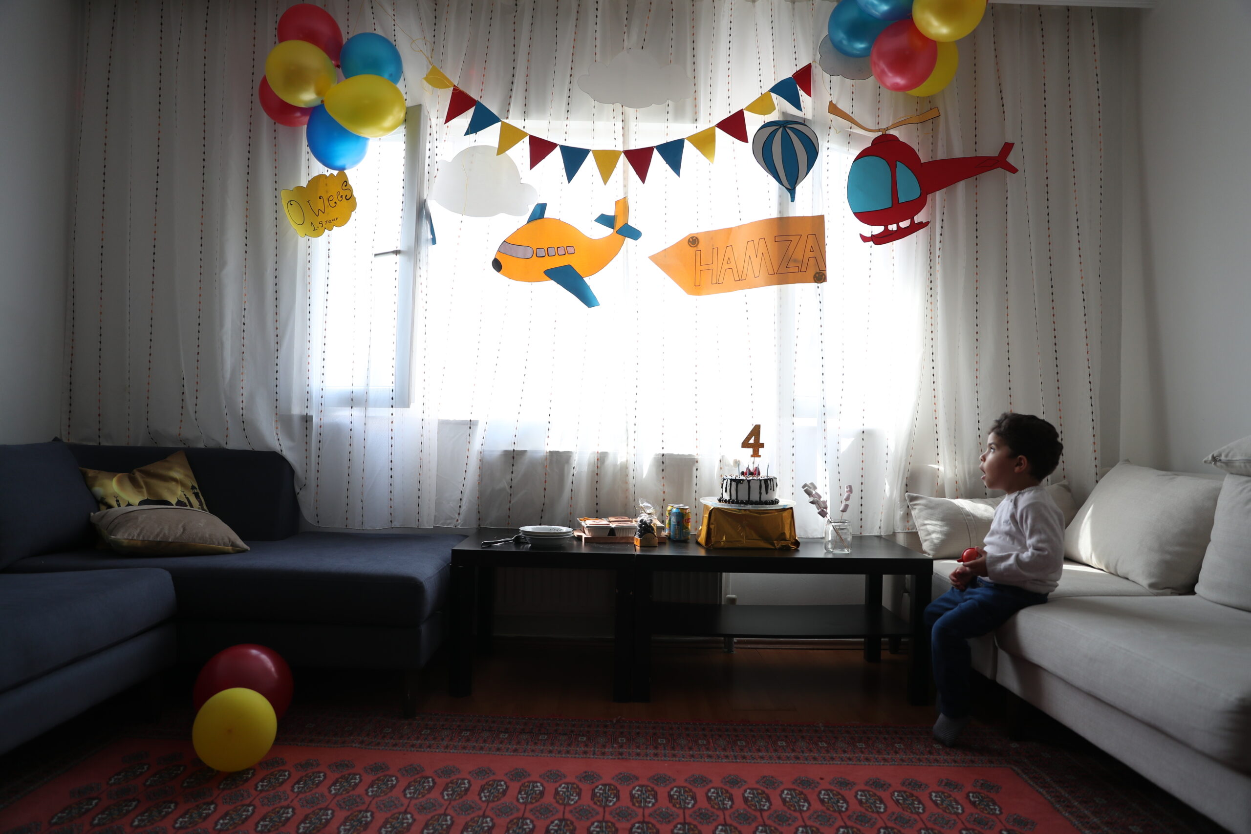 A young boys sits in a living room with decorations for a 4th birthday.