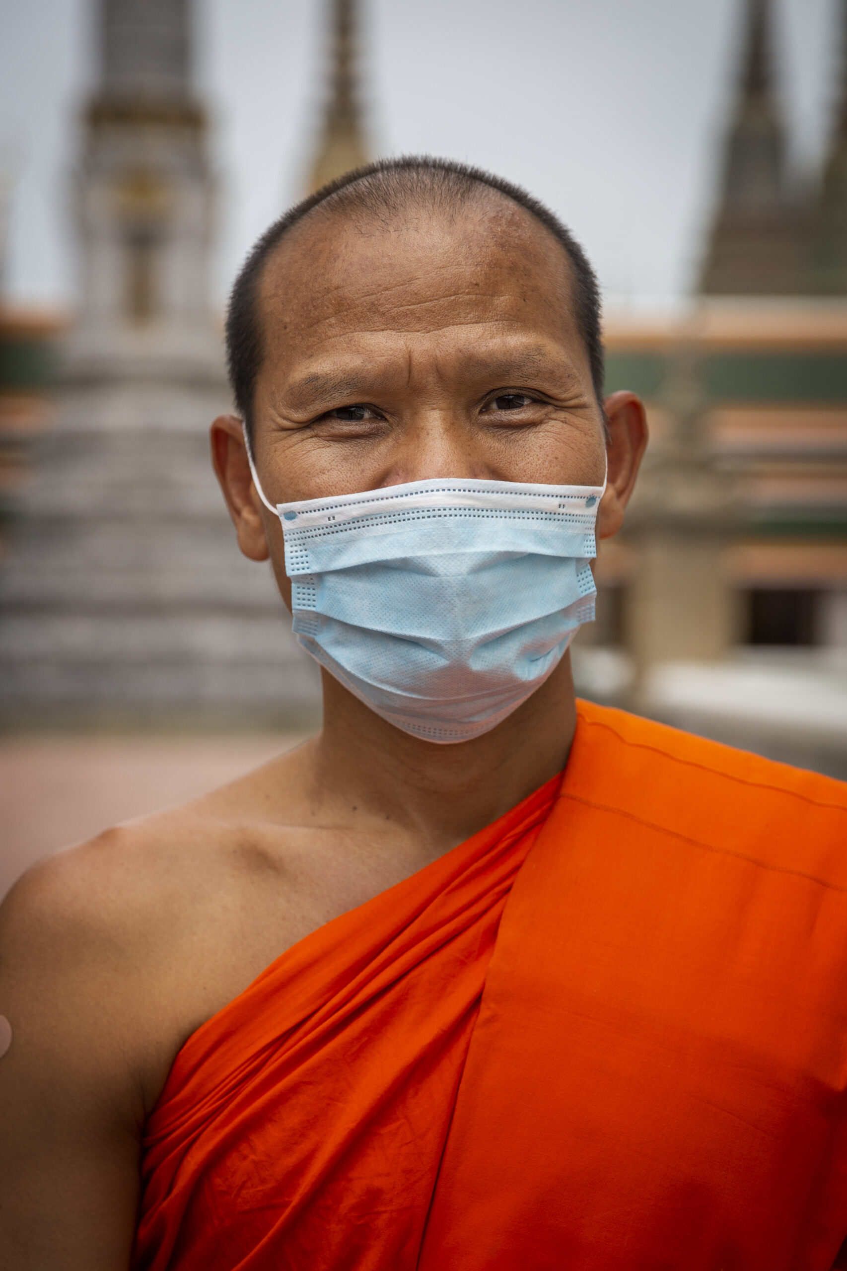 A monk wearing a mask looks on at the camera. 