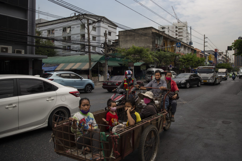 Four children are pulled by their parents in a rickshaw surrounded by cars in the road.