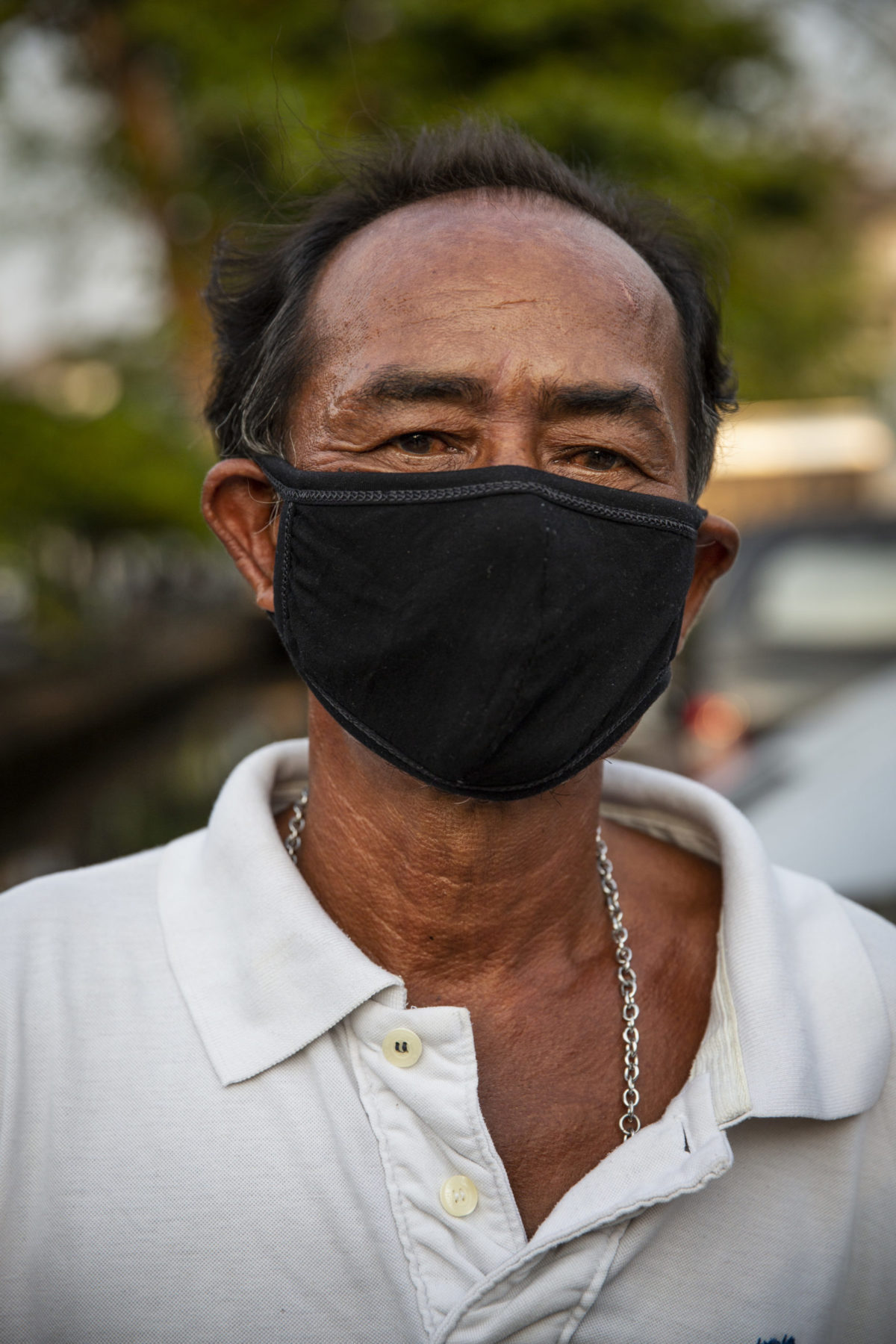 A person in a white polo and black face mask stands. 