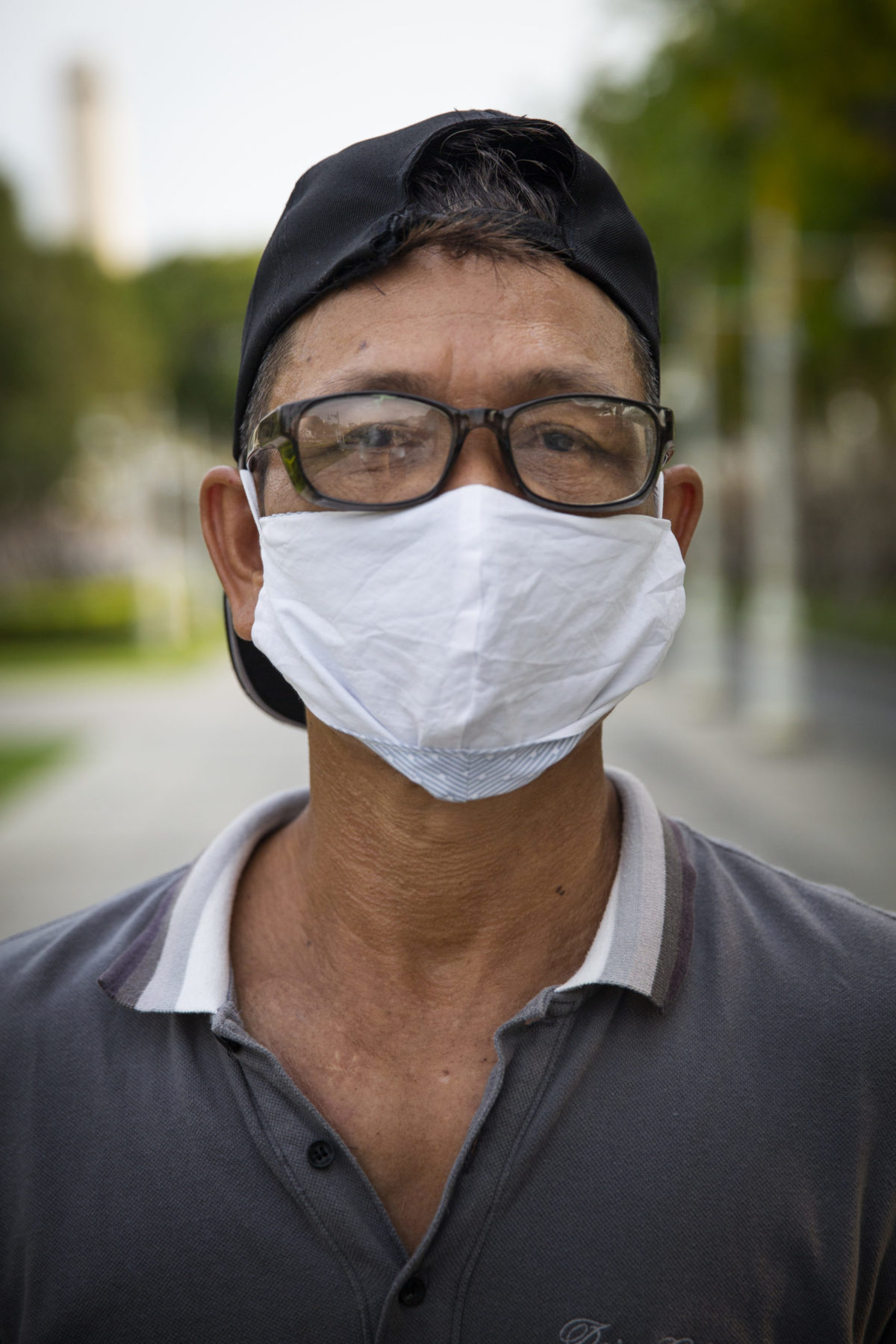 A young person wears a baseball cap, glasses, and a mask. 