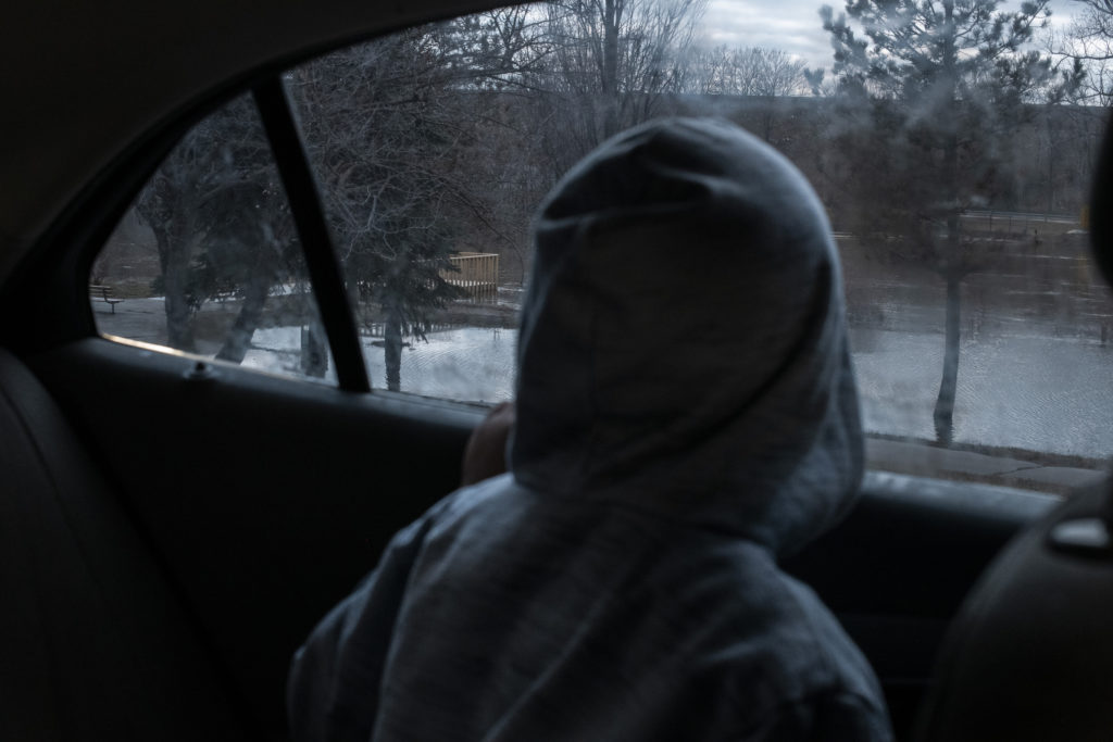 A child in a grey hoodie looks out of the window of a car onto a river. 
