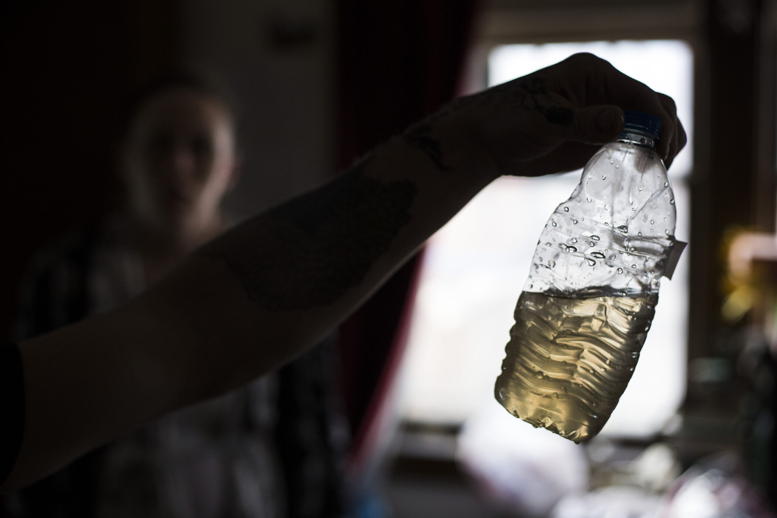 Close-up of person holding half full plastic bottle of yellow water