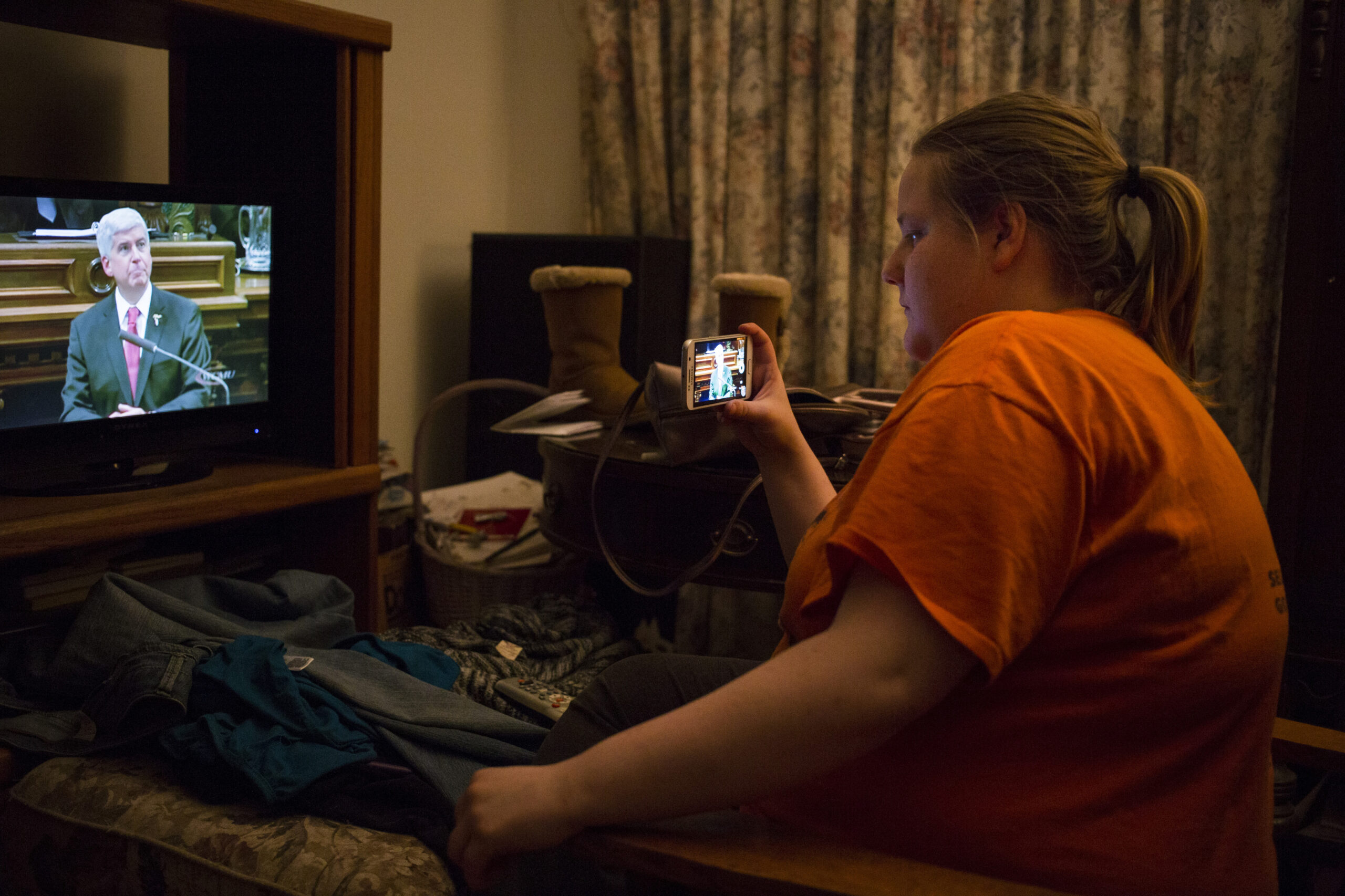 Woman recording Rick Snyder speaking on tv on her phone