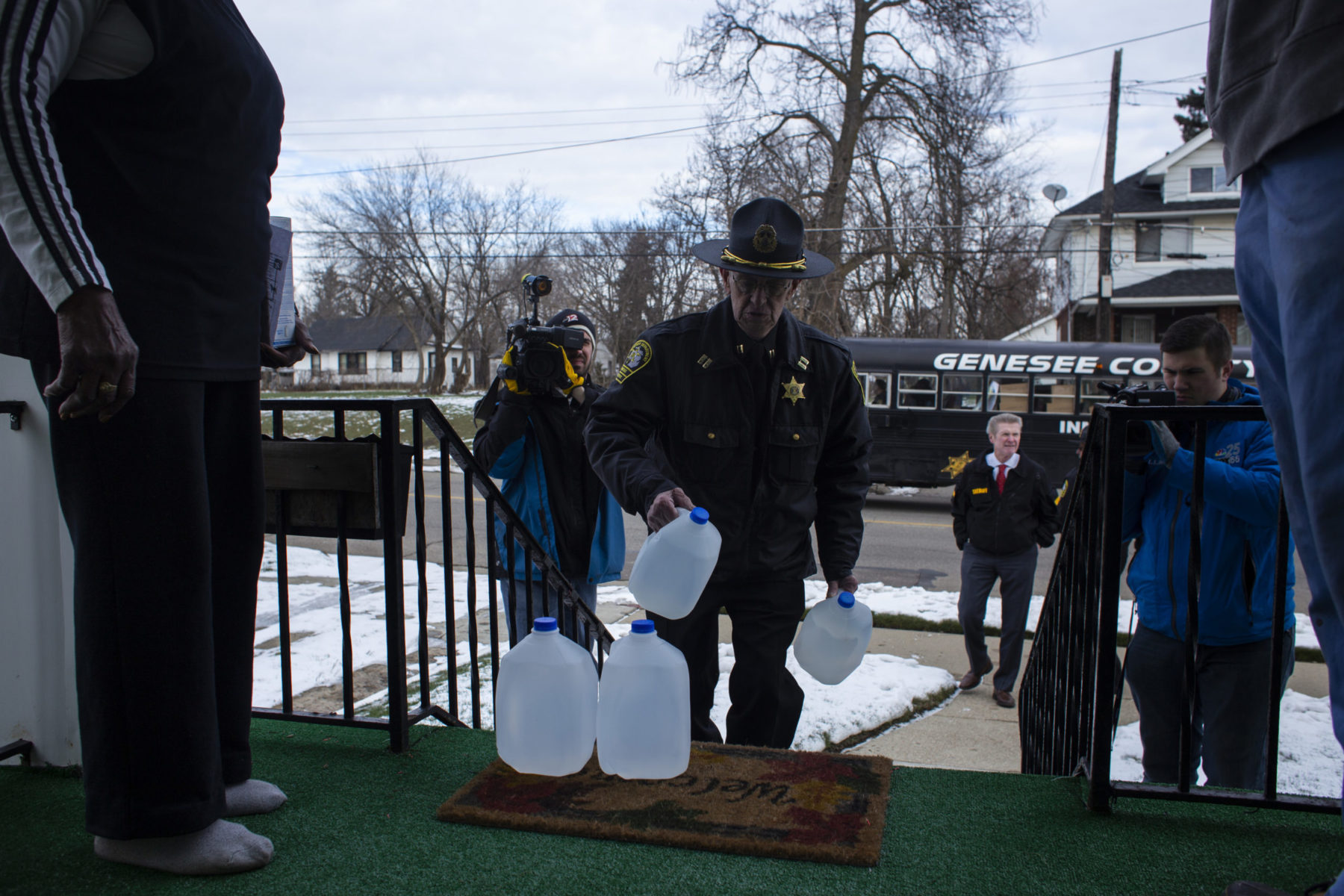 Person in police uniform carrying jugs of water and placing them on porch for photoshoot