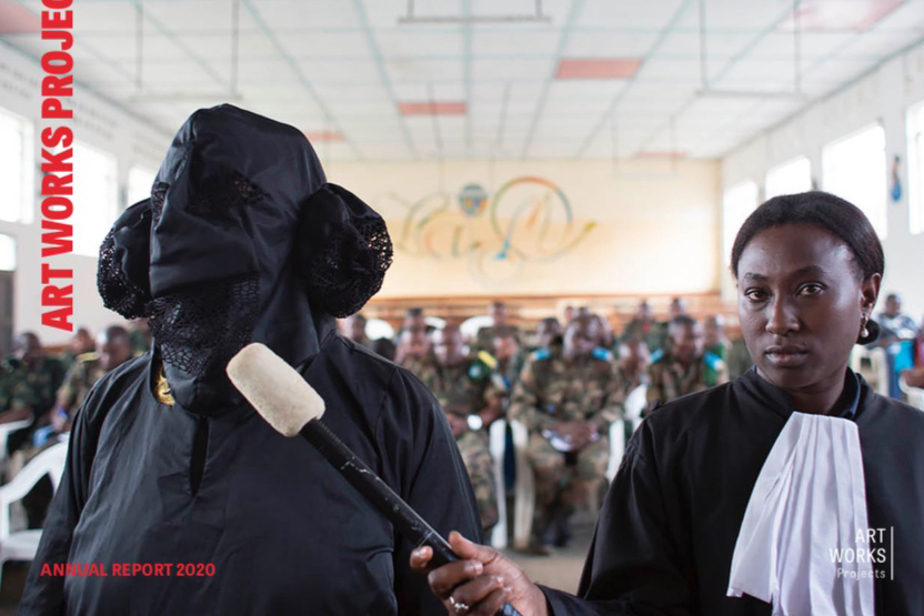 A person in judicial clothing holds a microphone to a person dressed in all black with their faced covered