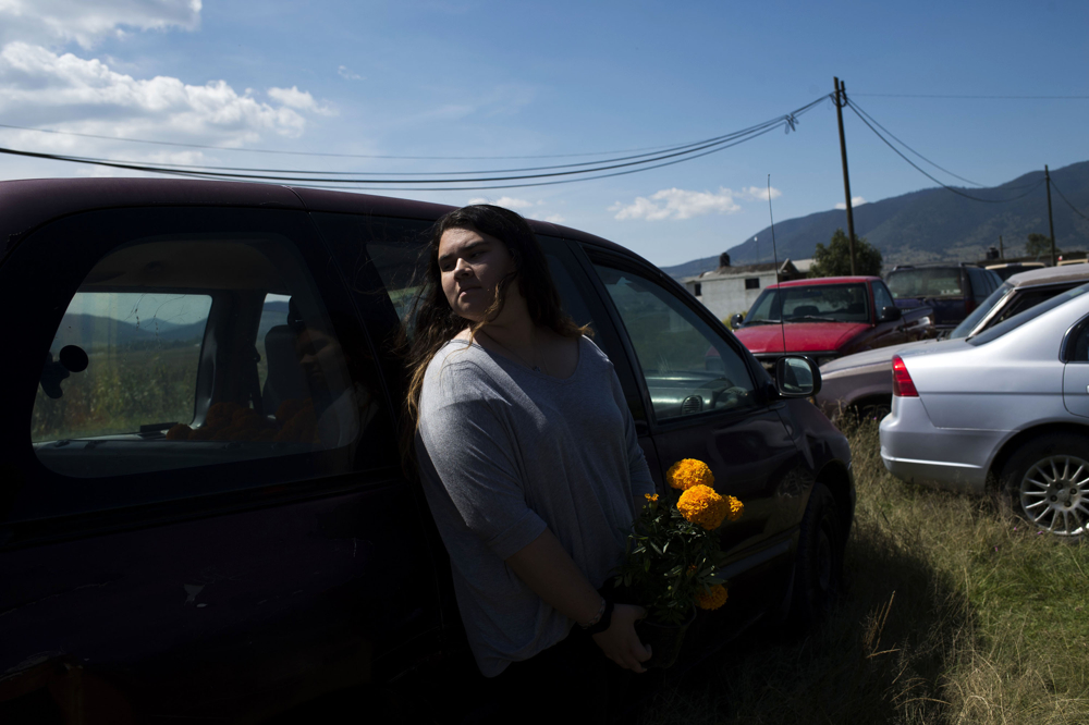 Lourdes Quintana-Salazar, 15, leans on a car holding flowers for her grandmother to bring to a funeral on Sunday, Oct. 22, 2017 outside of the cemetery in San Nicols, Mexico. Quintana-Salazar has been adjusting to life in Mexico, but misses her friends and life in the United States. Photo by Rachel Woolf.