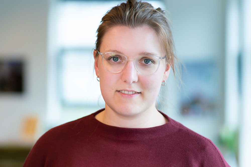 Anne Schroeter is smiling and wearing clear framed glasses and a maroon sweater