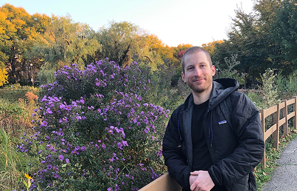 Caleb stands in front of purple and yellow flowers in a park