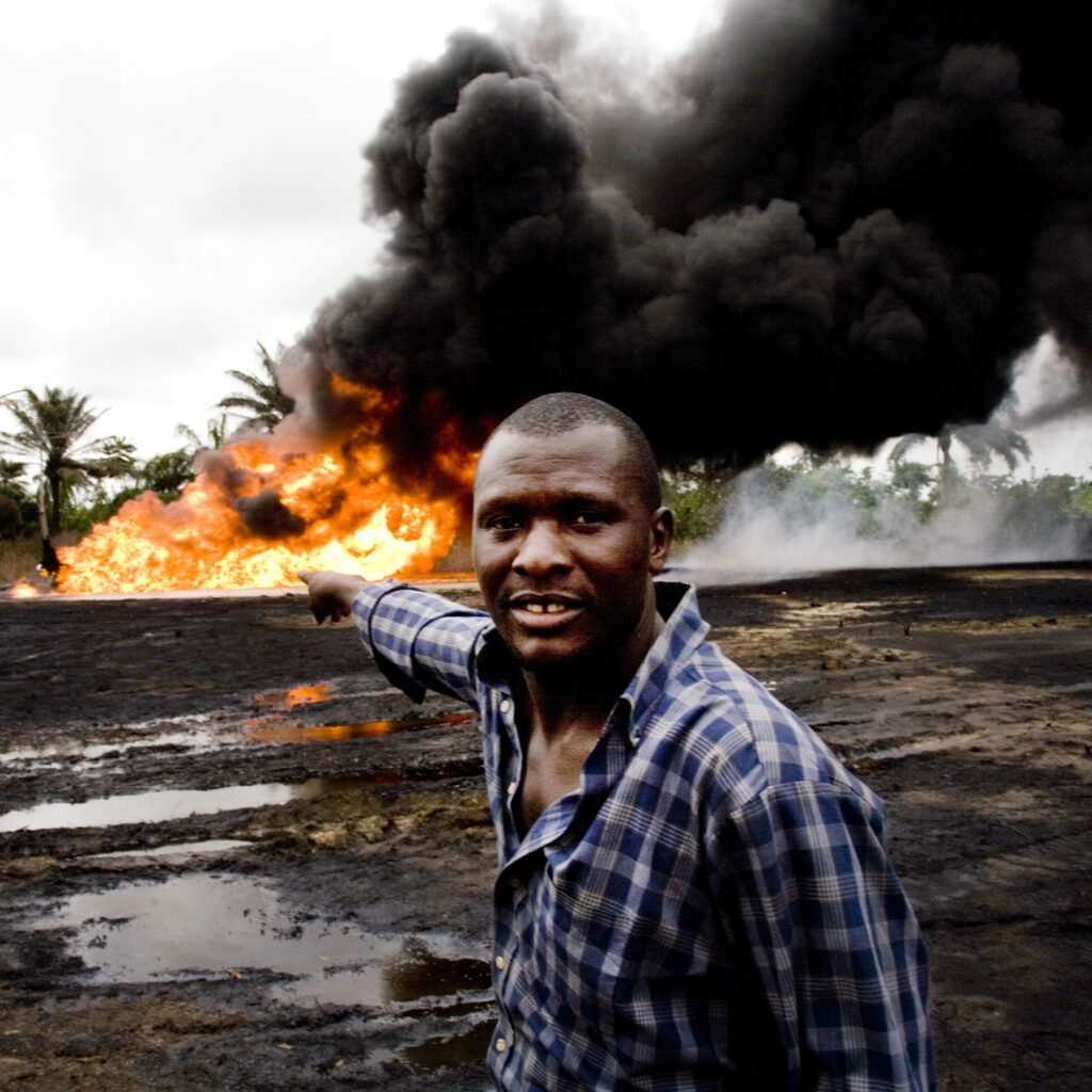 In the Ogoniland village of Kpean, an oil wellhead that had been leaking for weeks has turned into a raging inferno. The local youths keep watch, waiting for Shell to come and put the fire out. This is an environmental disaster for the local people, as it effects their crops, their water and air.