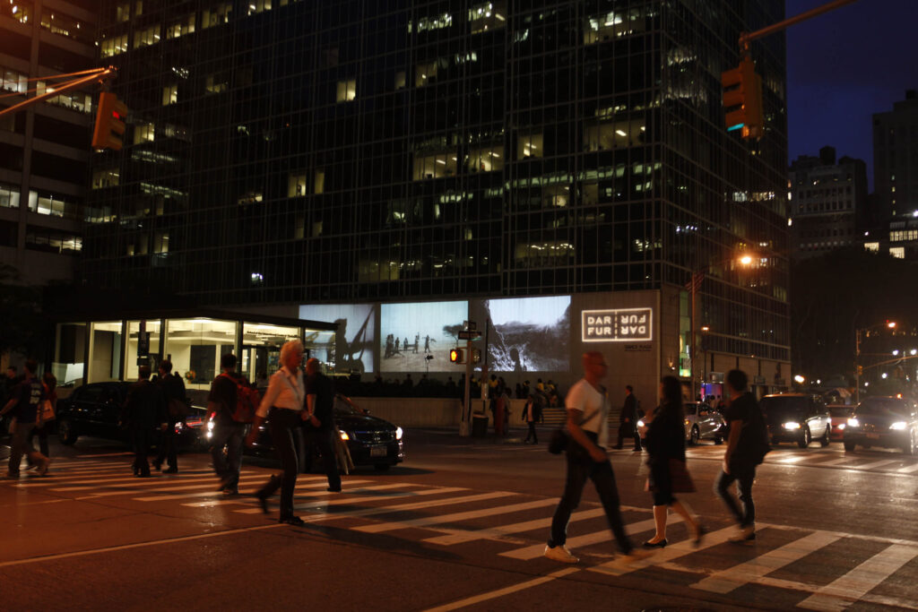 Photo of people walking in front of the New York Historical Society building with a projected image on its exterior walls