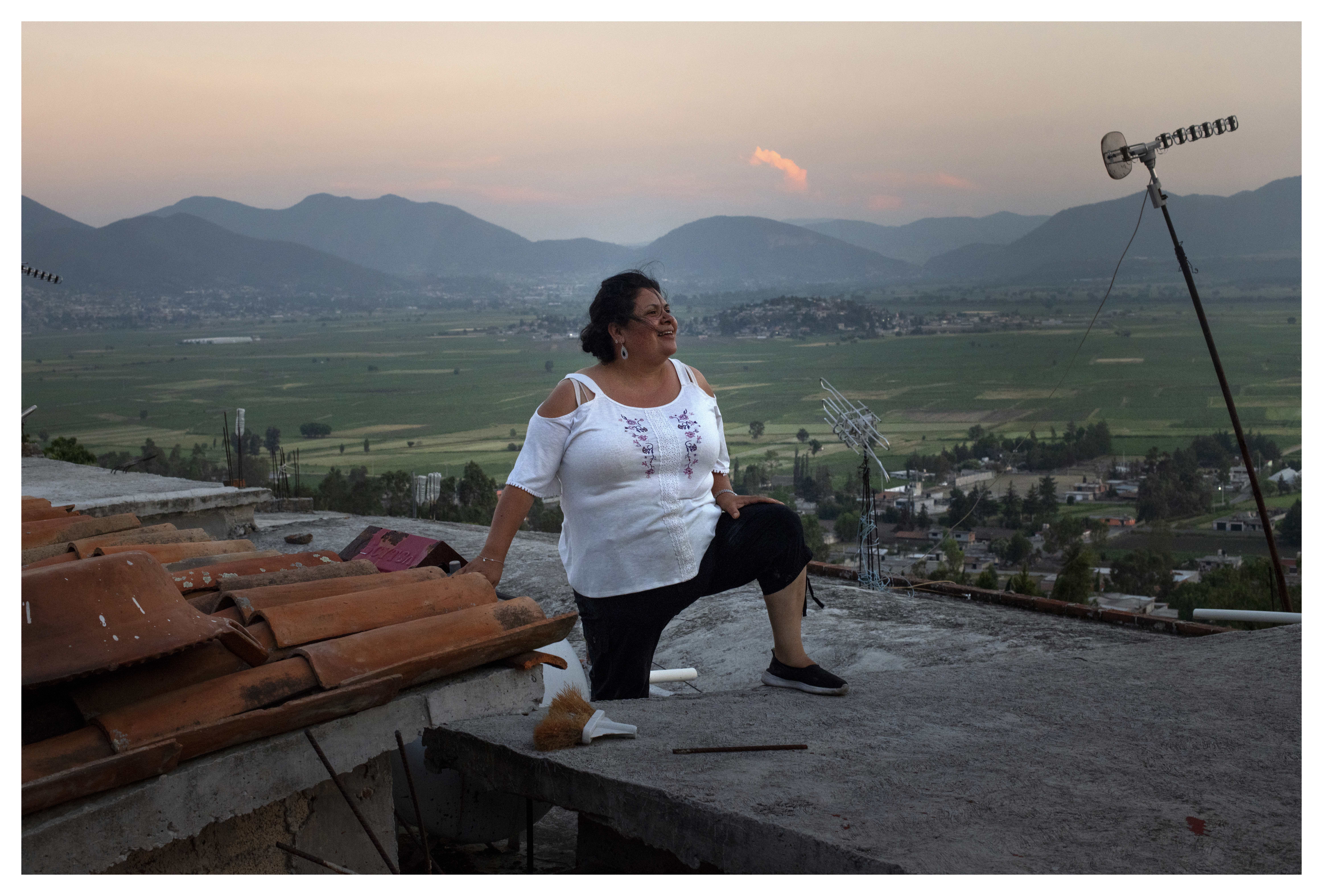 Lourdes Salazar Bautista looks up and smiles as she stands on the roof on Friday, June 1, 2018 at the house she grew up in, in San Nicols, Mexico. When Salazar Bautista was growing up, she used to think the mountains in the background were "the end of the world." Photo by Rachel Woolf for Deported.